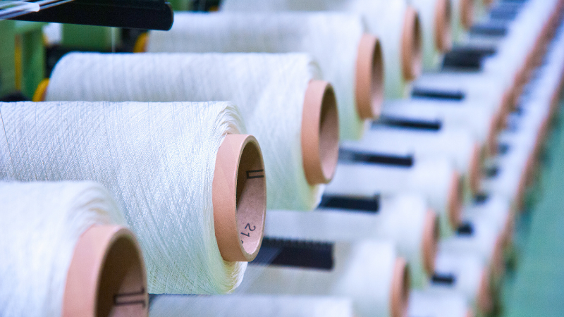 Close-up of spools of white yarn on a textile machine.
