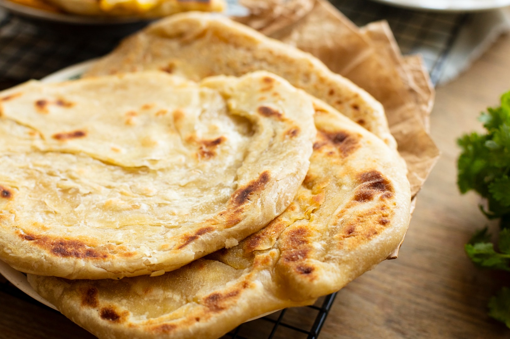 A serving of Roti Prata flatbreads on a plate next to a bowl filled with assorted vegetables.
