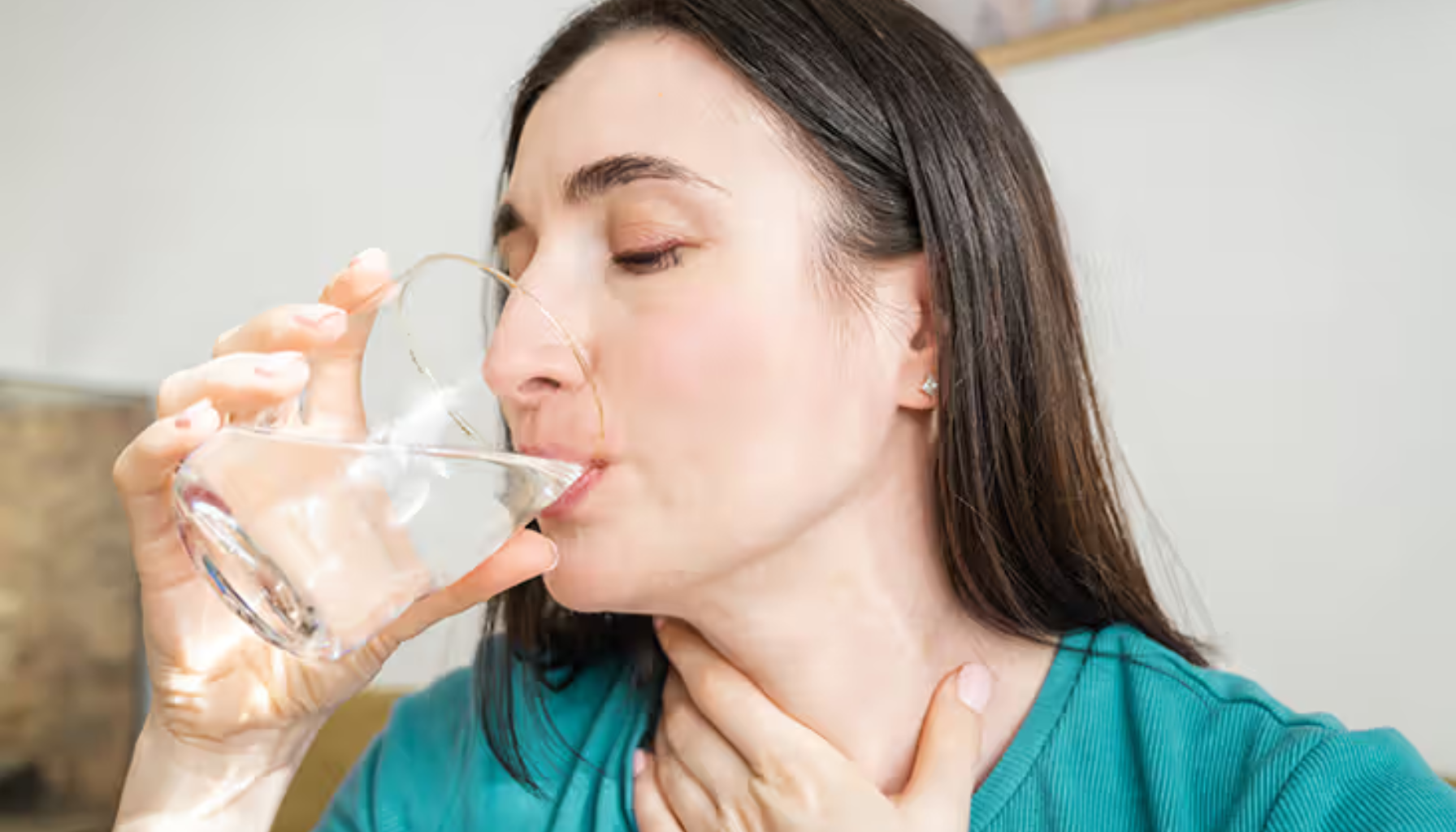 Kvinne drikker vann og holder seg på halsen, muligens for å lindre ubehag eller irritasjon i halsen.