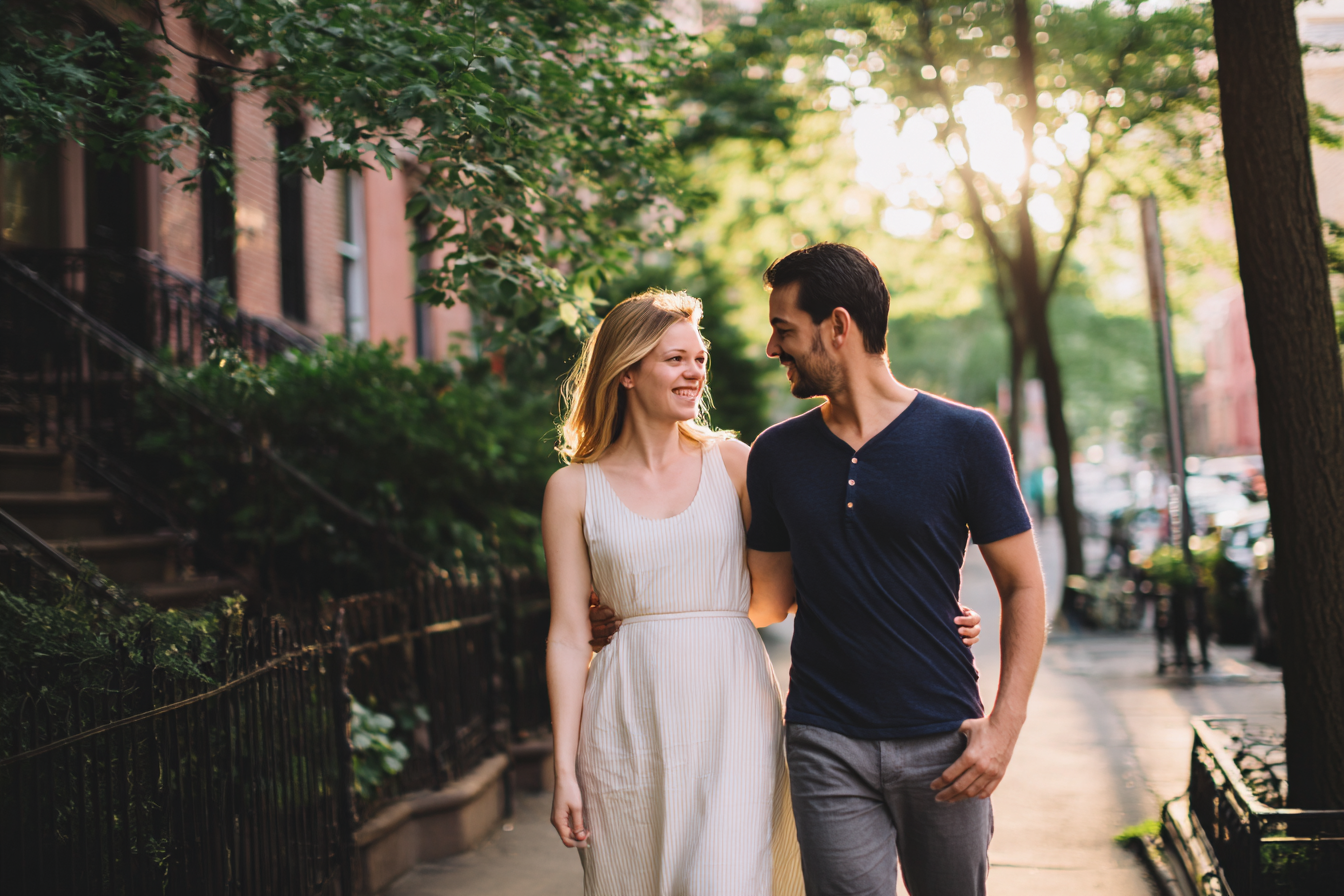 Attractive young heterosexual couple walking together on a West Village street with a small grounding touch between them, representing the integrative Gottman, EFT, and Schema Therapy approach at New York Therapy for couples whose work spans communication, attachment, and lifelong patterns.
