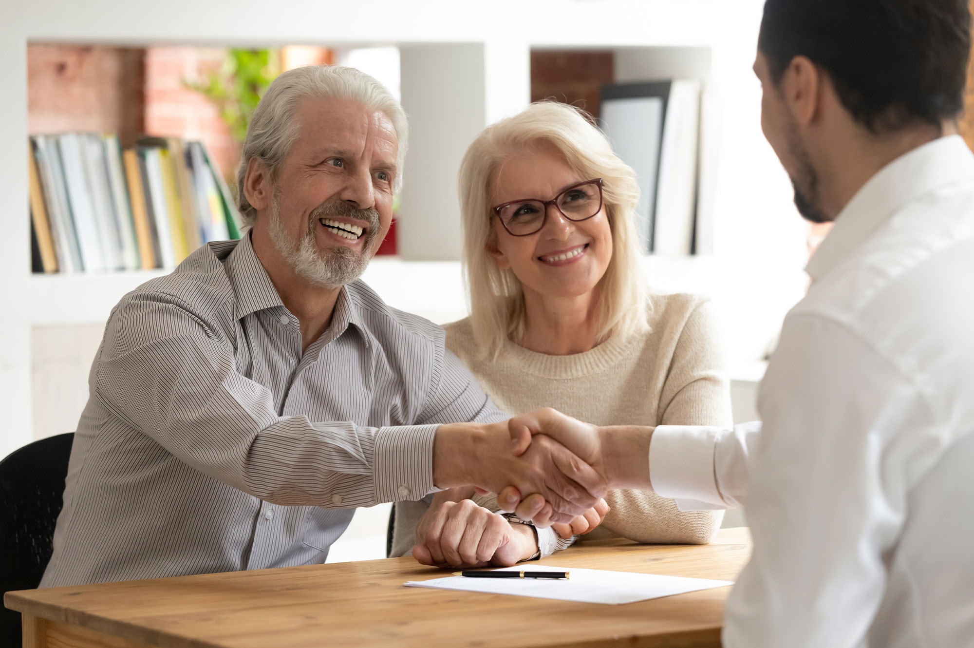 Smiling older couple shaking hands with a real estate advisor after a successful property trust agreement