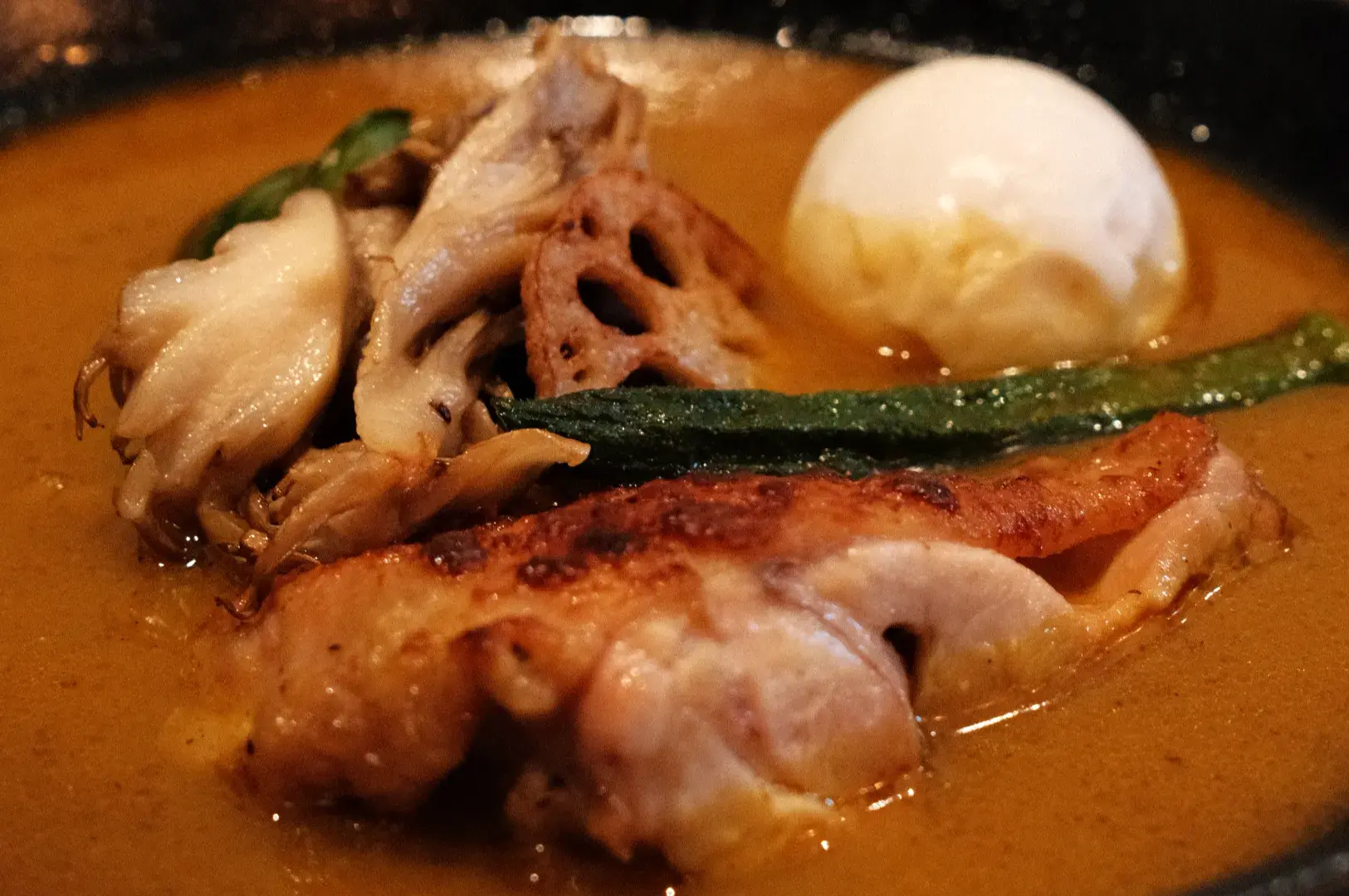 A bowl of rich, creamy curry with pieces of chicken, mushrooms, fried lotus root, and a soft-boiled egg.