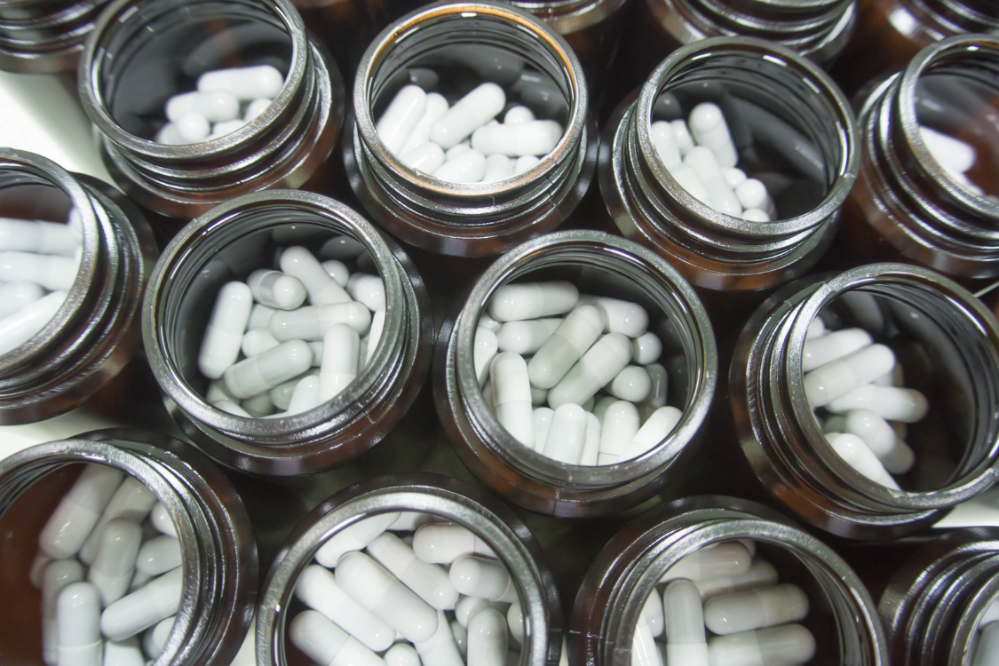 White supplement capsules in brown GMP-compliant bottles ready for packaging