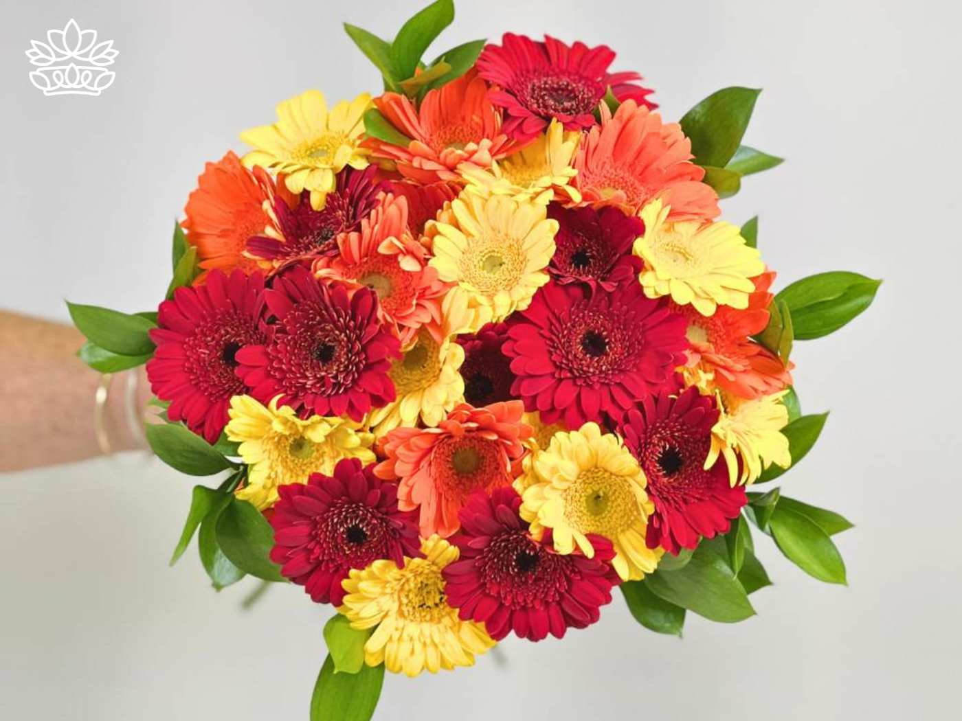 A vibrant bouquet of Gerbera daisies in shades of red, orange, and yellow, complemented by lush green foliage. Fabulous Flowers and Gifts. Gerberas Collection. Delivered with Heart.