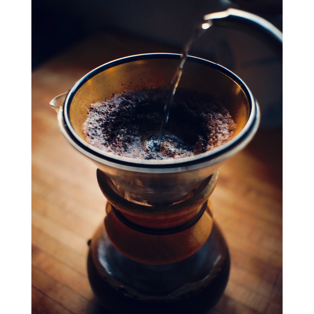 A person pouring hot water over freshly ground coffee beans in a pour over coffee maker