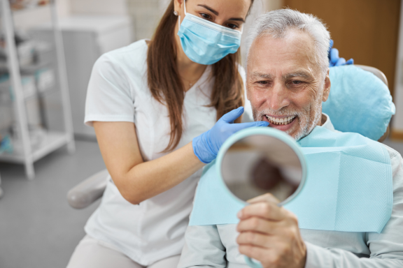 senior male smiles in mirror at new dental implant to complete his smile