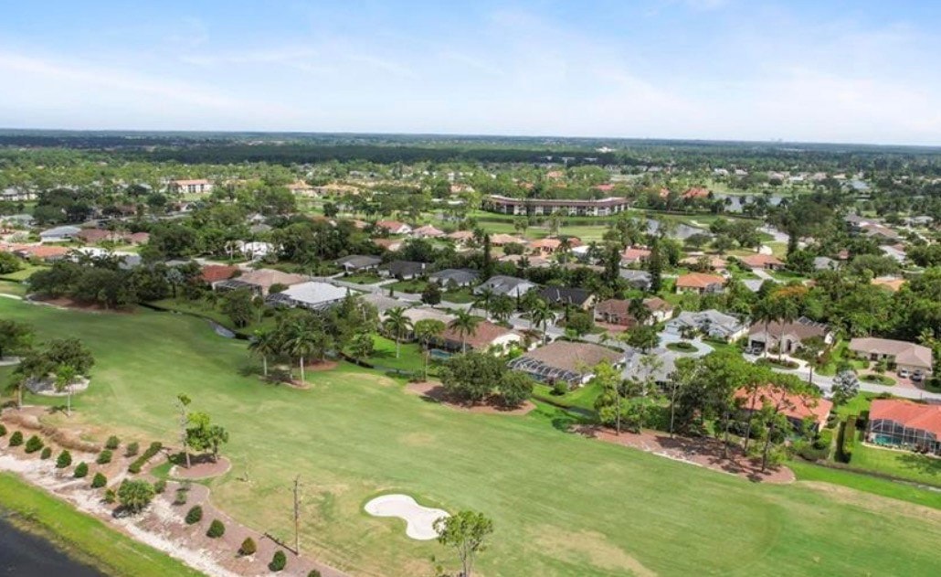 The image depicts a scenic golf course fairway at Lely Resort in Naples, Florida, bordered by lush palm trees and shimmering water hazards, creating a beautiful and inviting atmosphere for residents and visitors alike. This private country club setting offers a serene environment for golfers to enjoy their game while surrounded by nature.