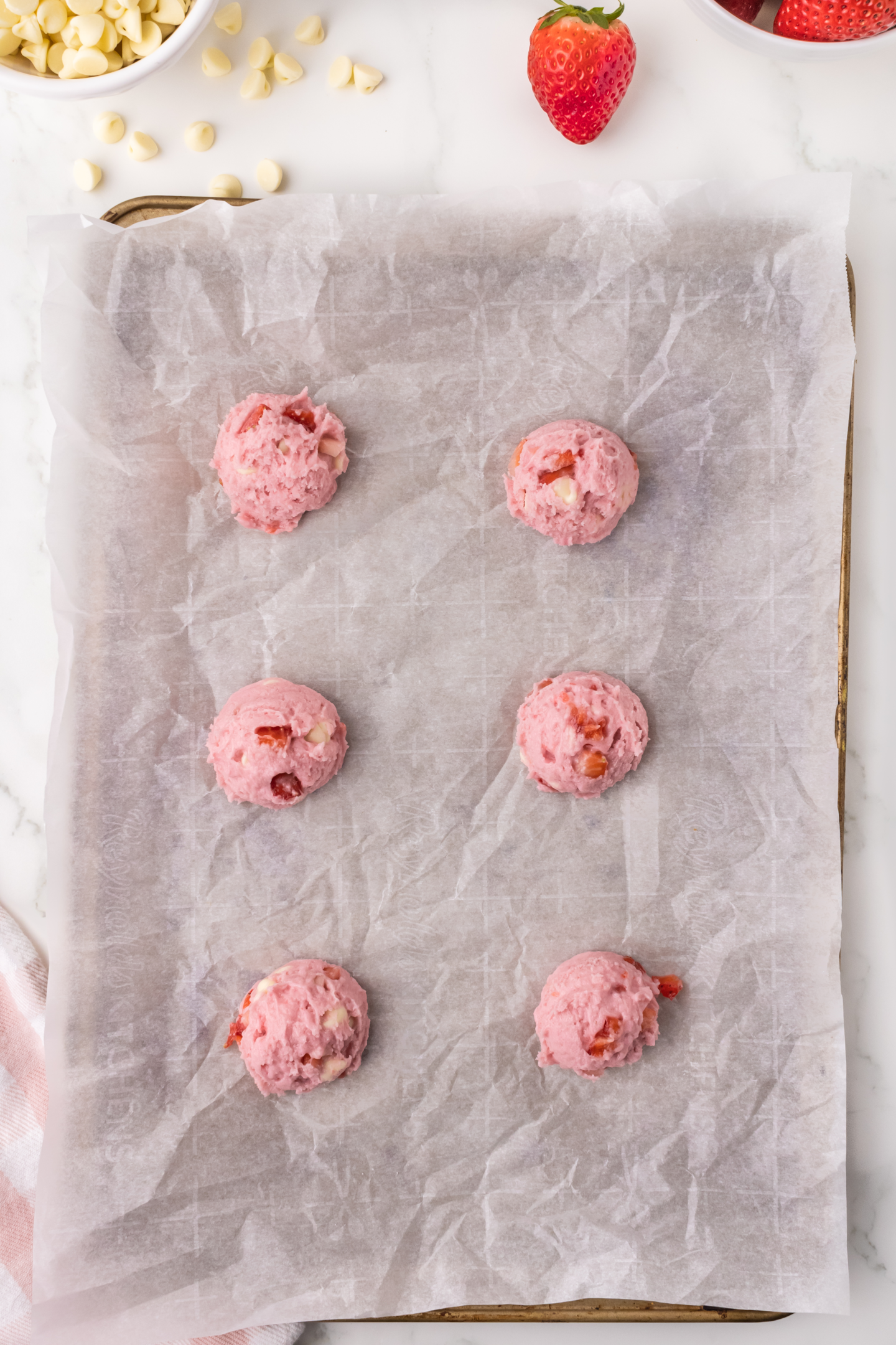 unbaked strawberry cookie dough balls on parchment paper baking sheet