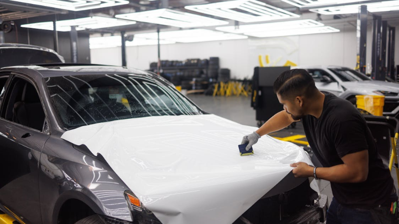 a mechanic using use squegee to remove bubbles from vinyl car wrap