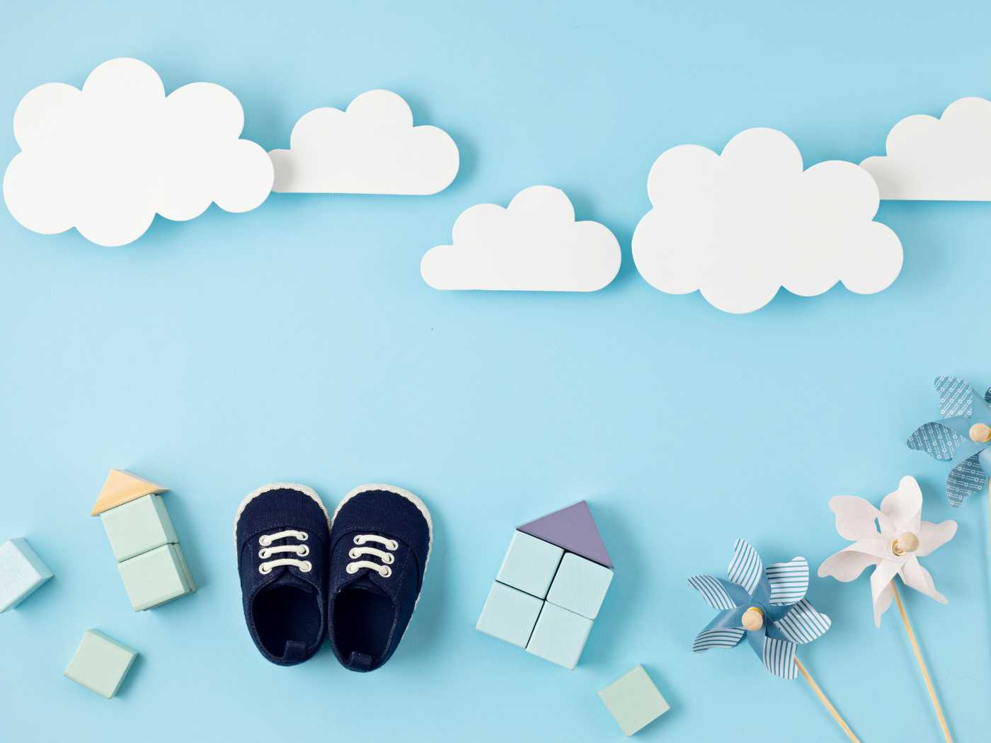 Creative gender reveal idea featuring a pair of navy blue baby shoes, wooden blocks, and pinwheels on a pastel blue background with white cloud cutouts, from the Gender Reveal Collection at Fabulous Flowers and Gifts.
