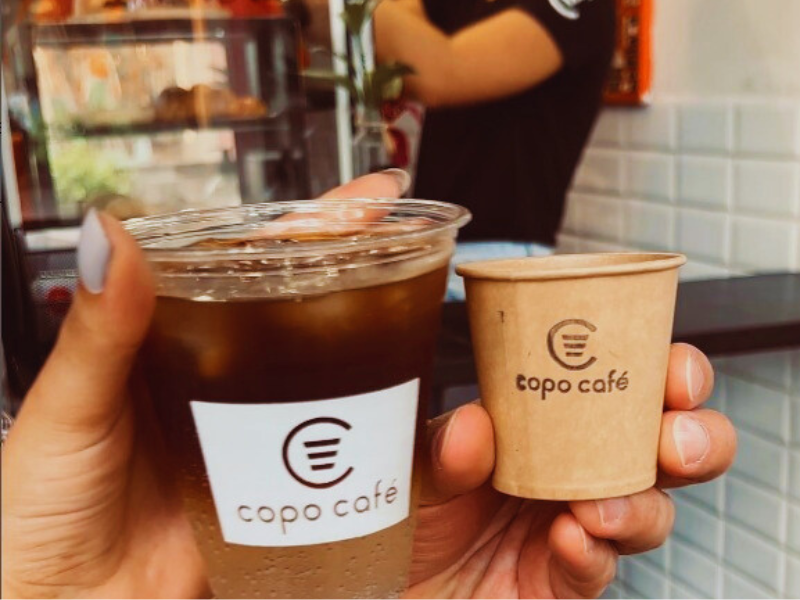 Copos de café para viagem em frente ao balcão da Copo Café em BH. Imagem: Reprodução Instagram. 