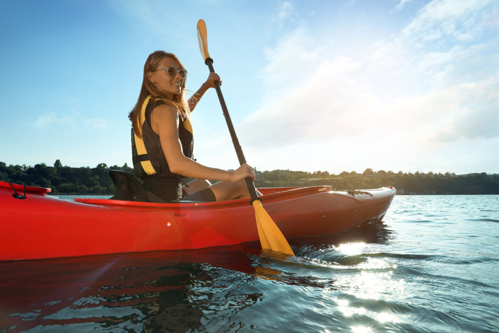 Young woman with blonde hair paddling a red kayak. 