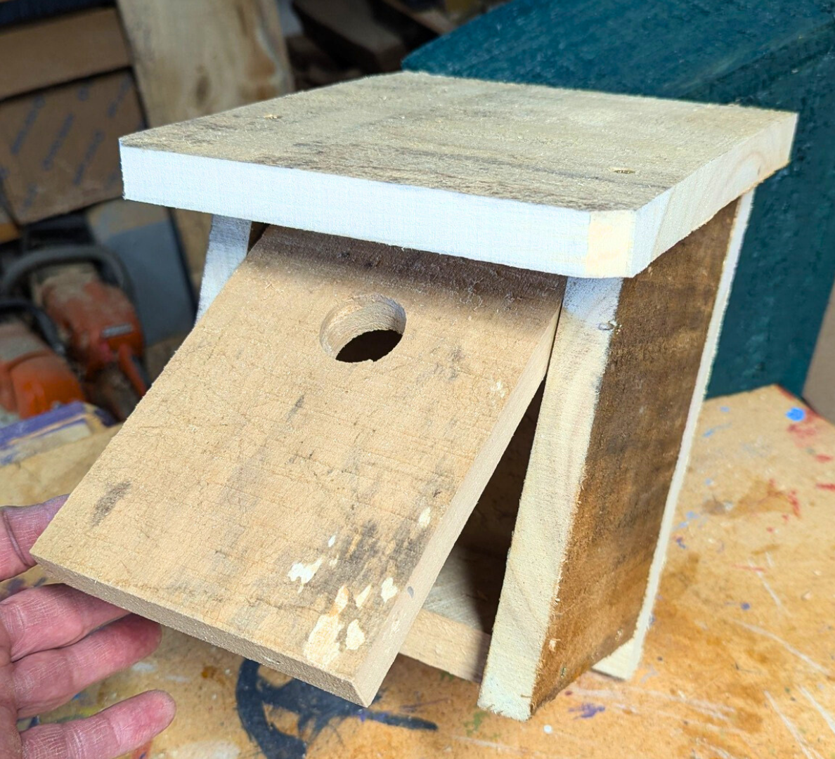 A rough-cut birdhouse in a workshop, made with nails and glue. 