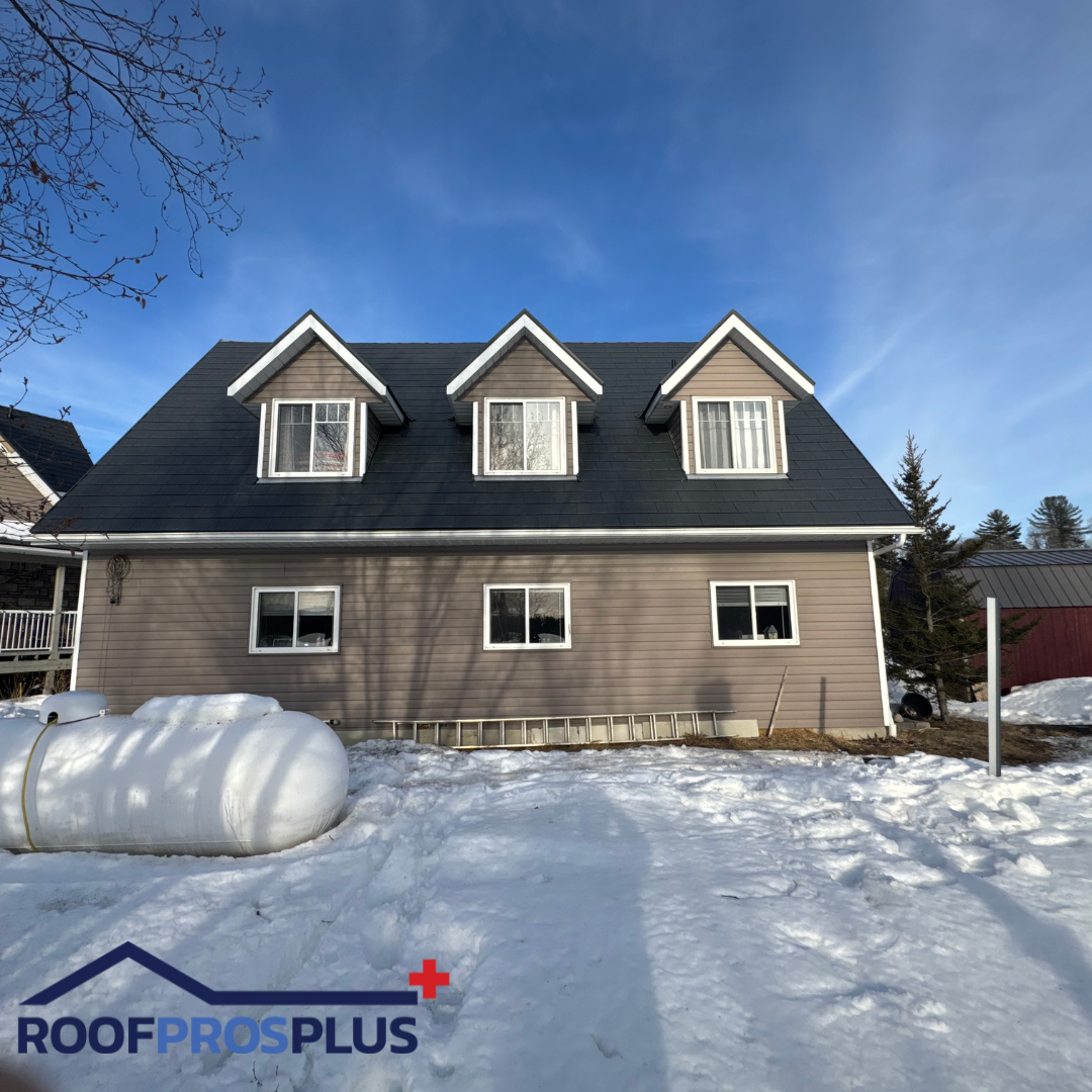 A house with a beautiful grey metal roof, set against a ground covered in fresh snow.

