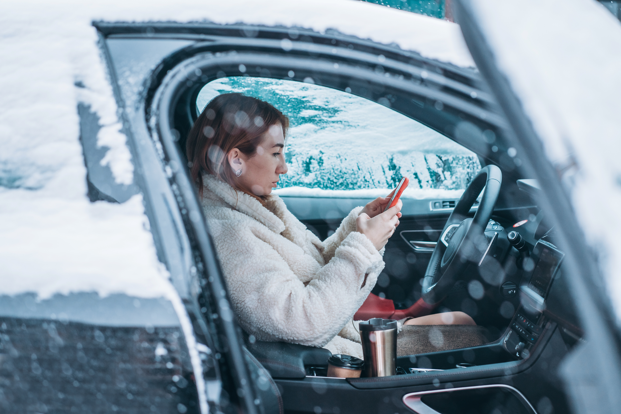 Woman holding mobile phone inside car, winter outside.