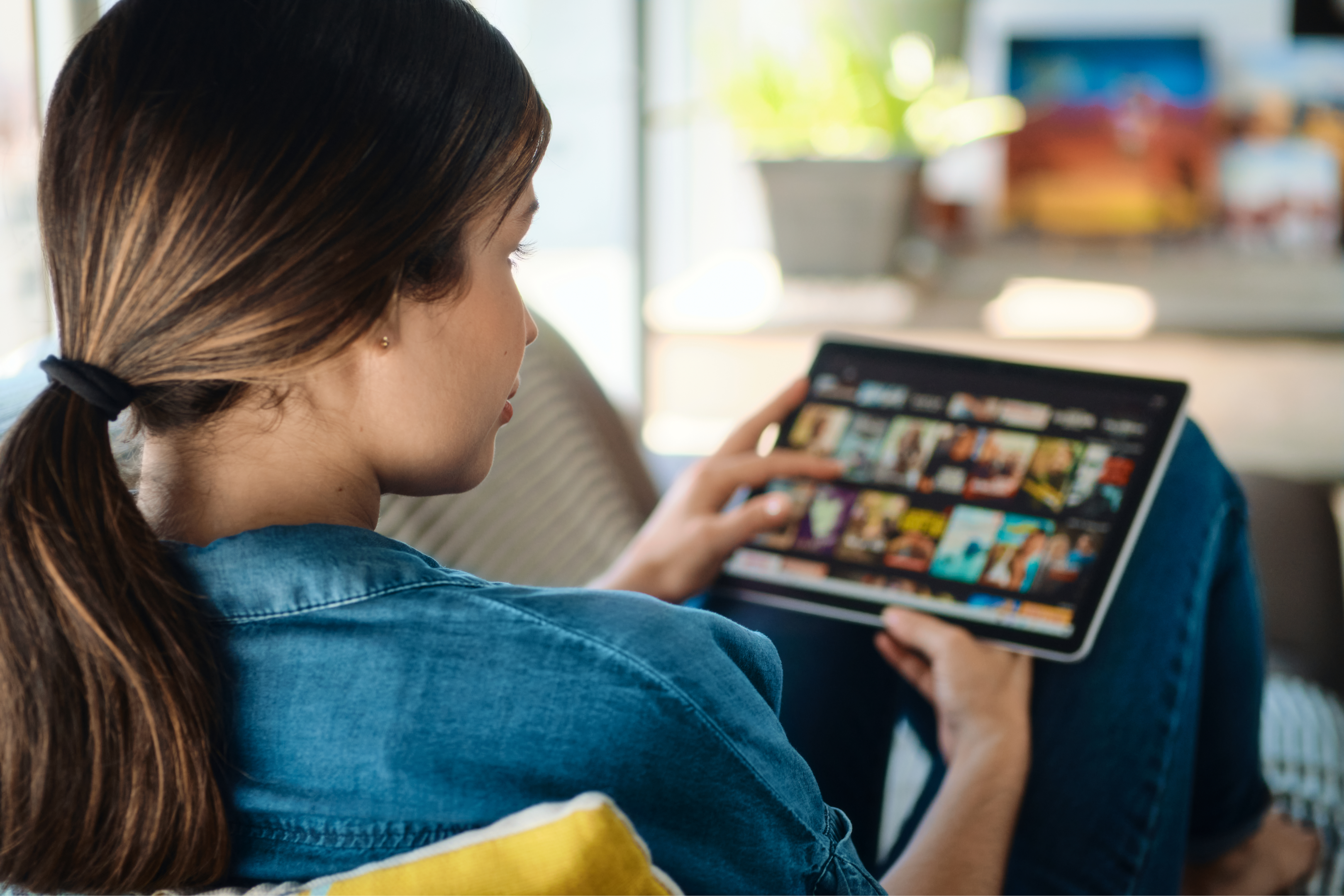 a woman browses a streaming interface on a tablet while sitting on her couch