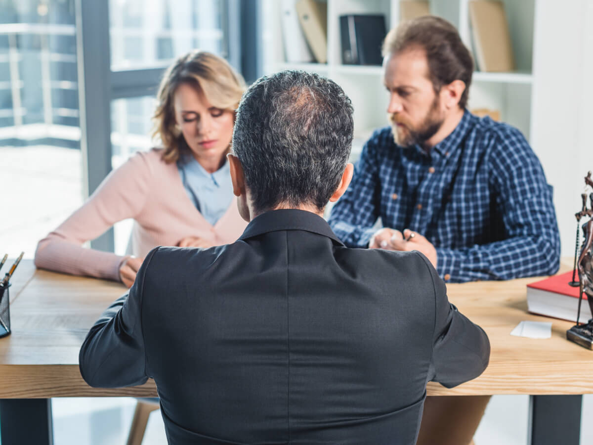 Couple sits at a table with their lawyer, reviewing documents and discussing