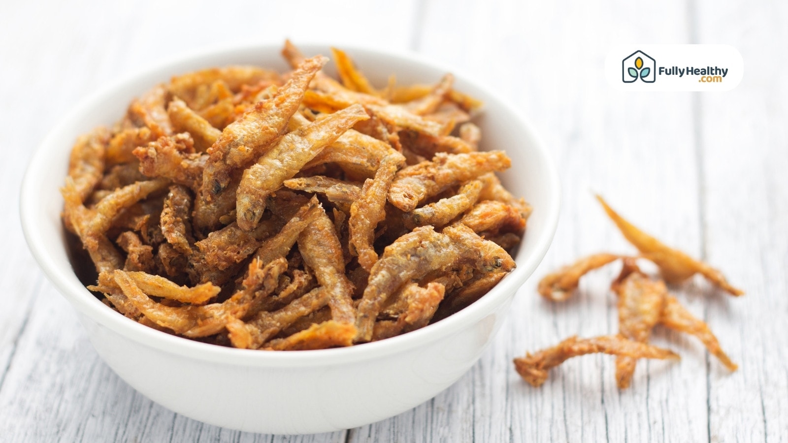 Crispy fried anchovies in white bowl on light wooden table