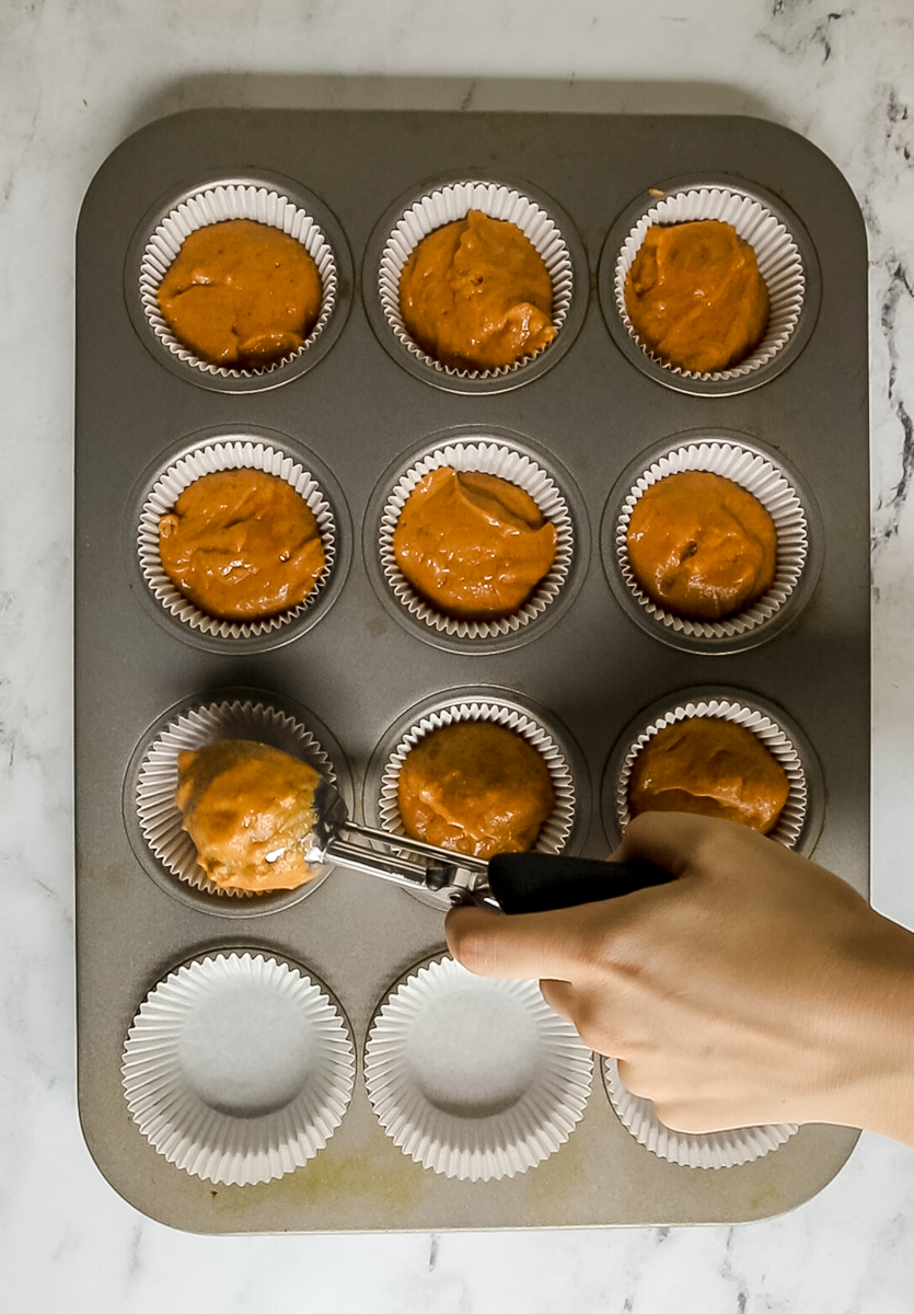 pumpkin batter being scooped into cupcake liners