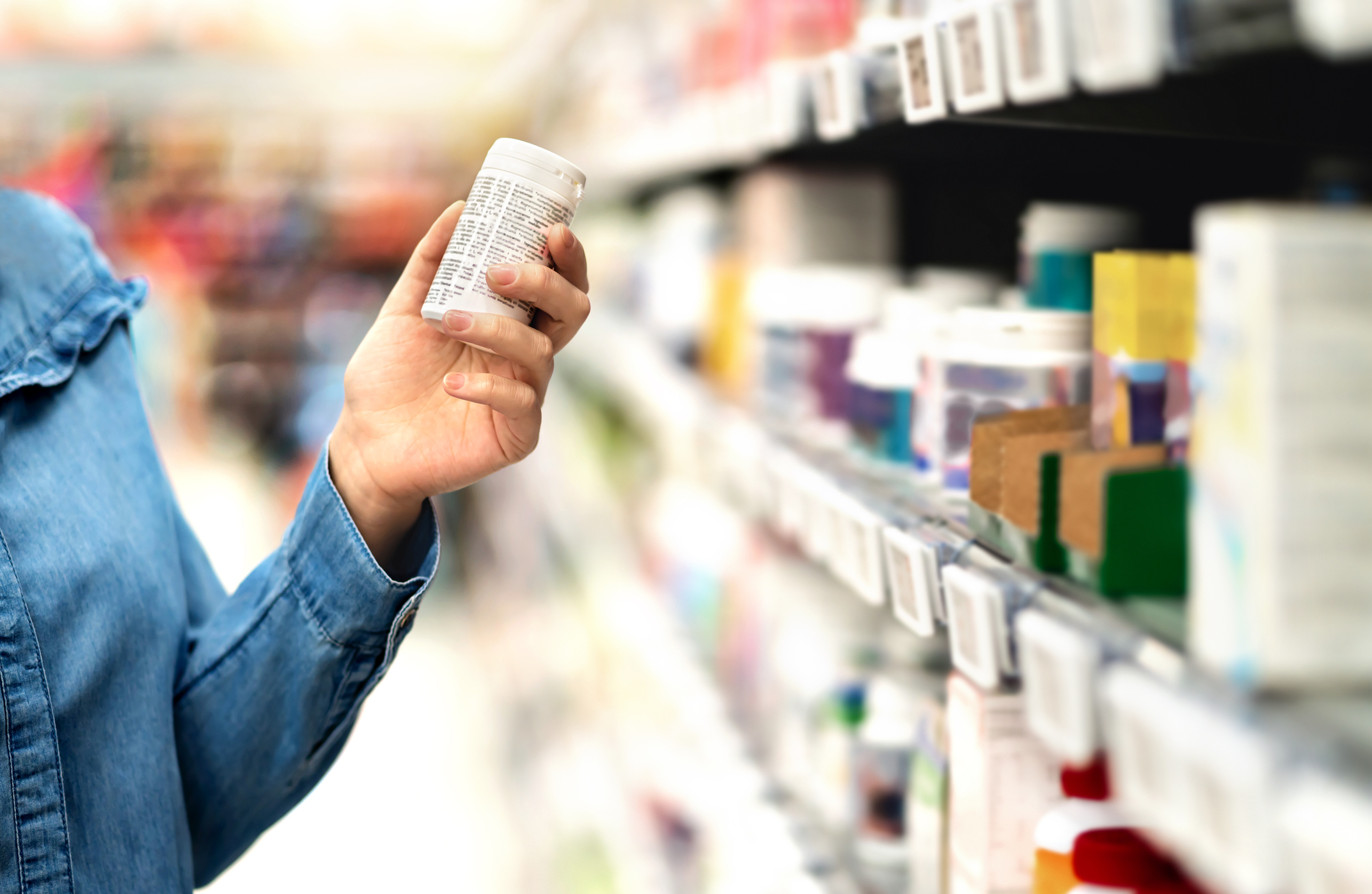 An image of a woman holding and reading a bottle of dietary supplements. 