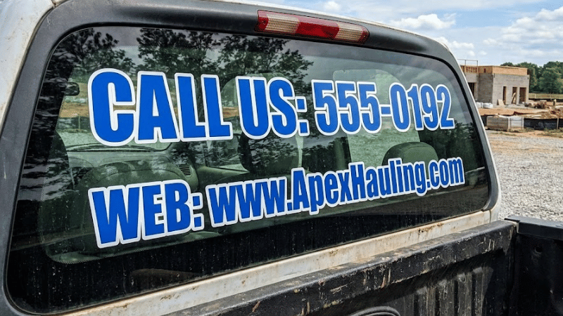 Phone numbers and websites decals are displayed on truck windows.