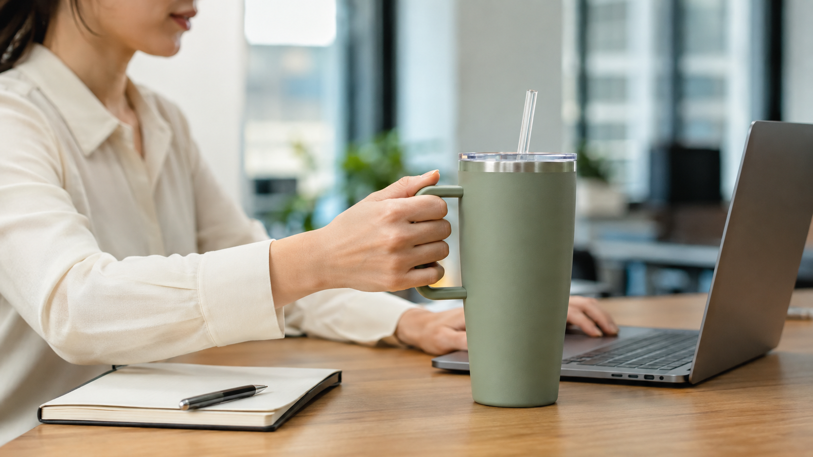 Office worker using a large handled tumbler with a straw for frequent upright drinking at a desk