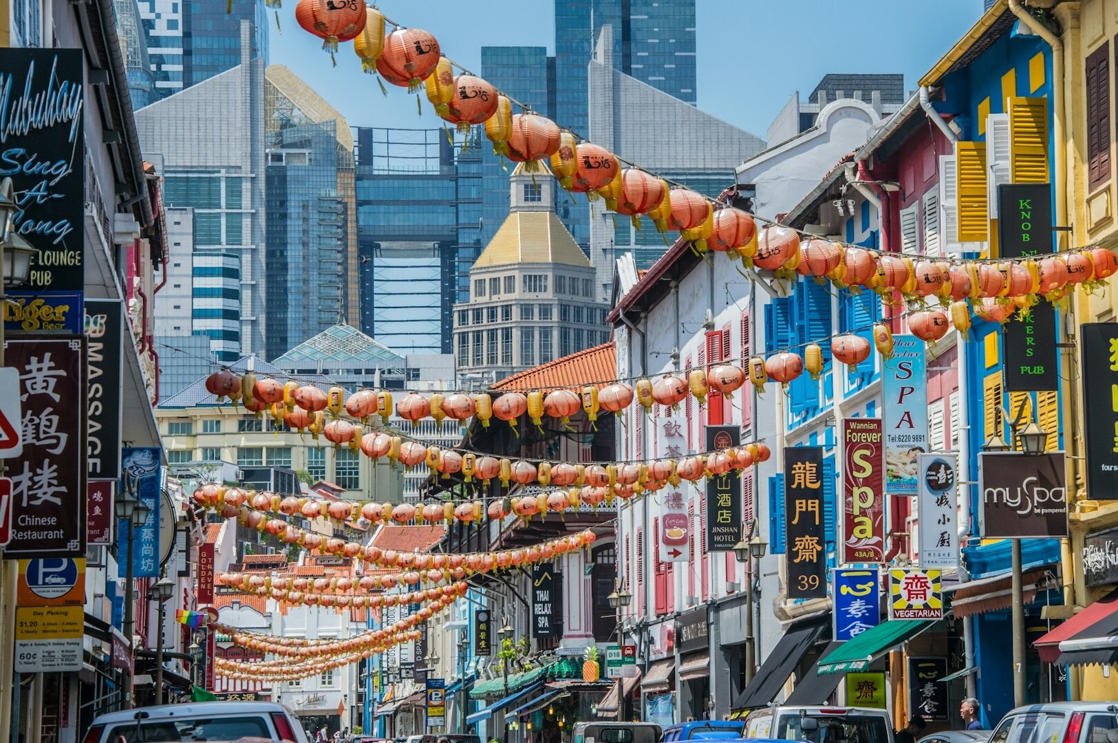 A vibrant street scene in Chinatown featuring cars and people strolling down the road.