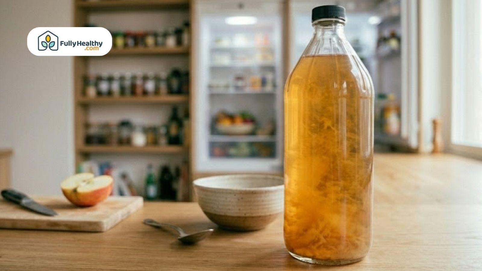 Raw apple cider vinegar with the vinegar mother sediment in a glass bottle on a kitchen table.