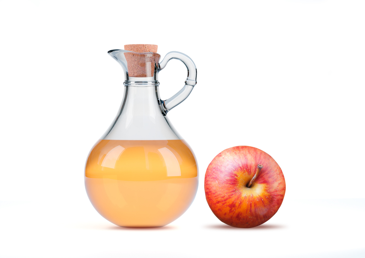 An image of a glass container of apple cider vinegar with an apple on a white background. 