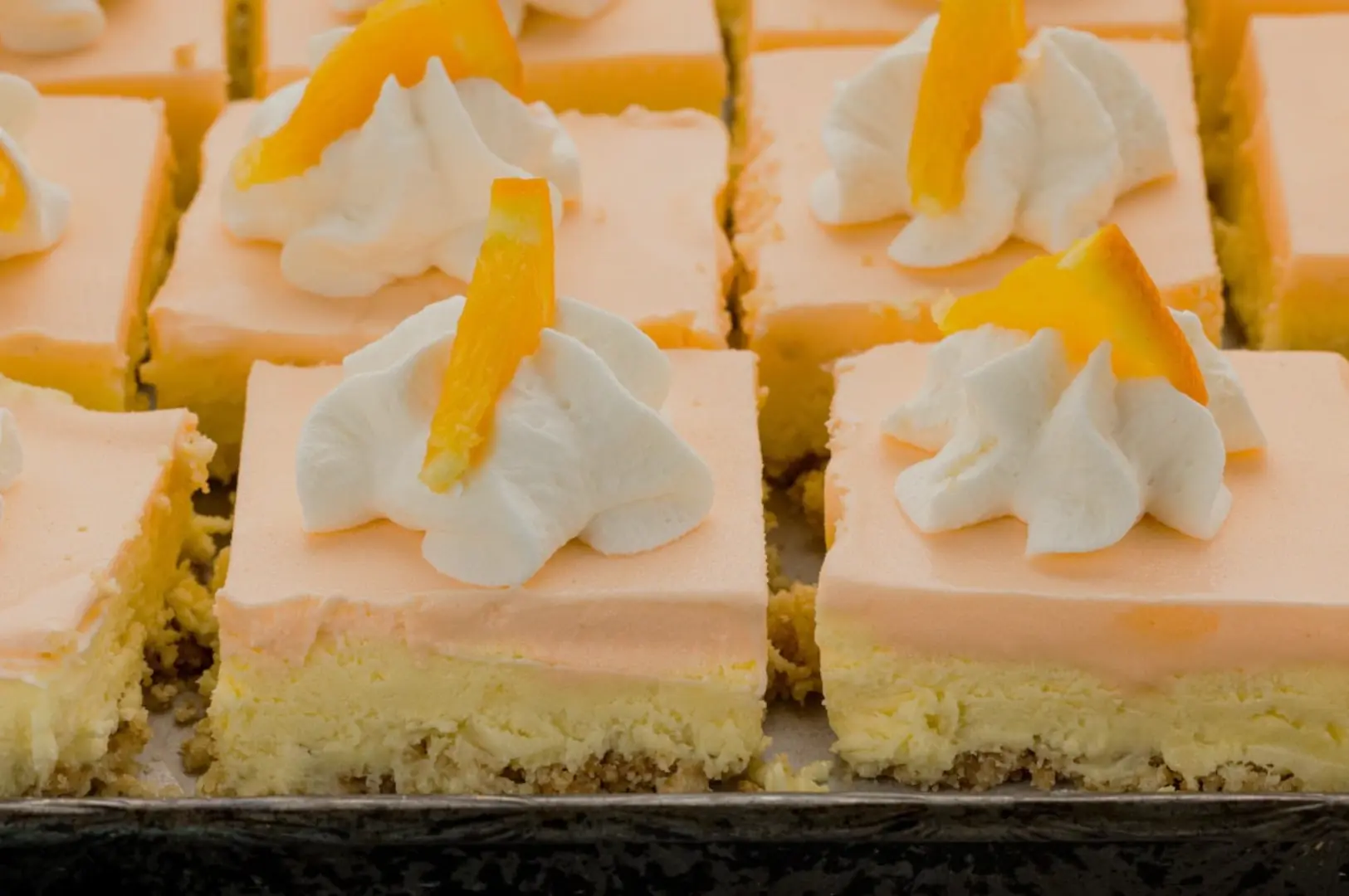 A close-up view of dessert squares topped with orange cream, whipped cream, and a slice of orange on each piece.