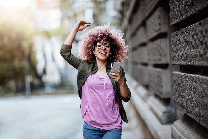 Cheerful young woman in a purple shirt bounding down the street listening to music. 