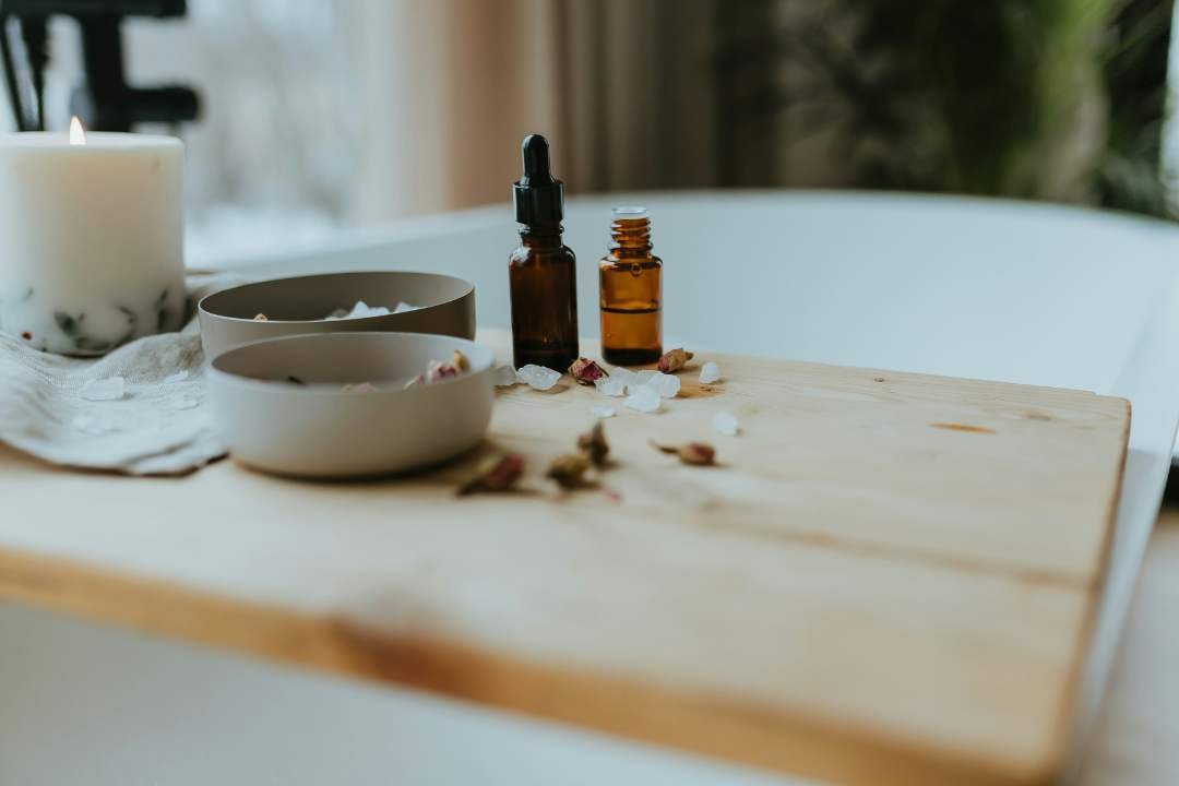 Essential oil bottles and candle on a wooden tray beside a tub, creating a serene spa ambiance.