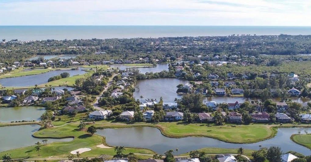 The image showcases a semi-private golf course with lush green fairways and a serene lake, complemented by an elegant clubhouse in the background. This idyllic setting reflects the relaxed island atmosphere of Sanibel Island, perfect for enjoying the extraordinary living space and outdoor lifestyle.