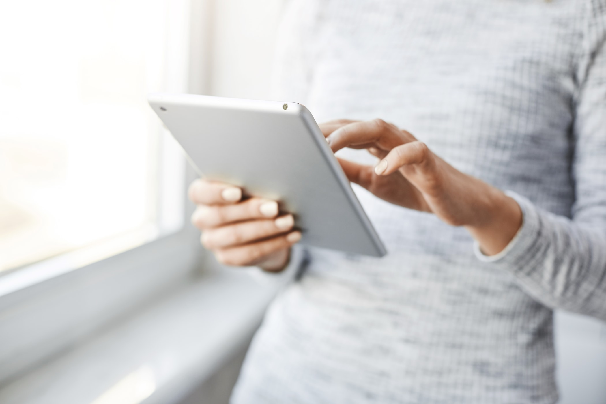 Stehende Frau mit grau-meliertem Kleid liest auf dem Tablet