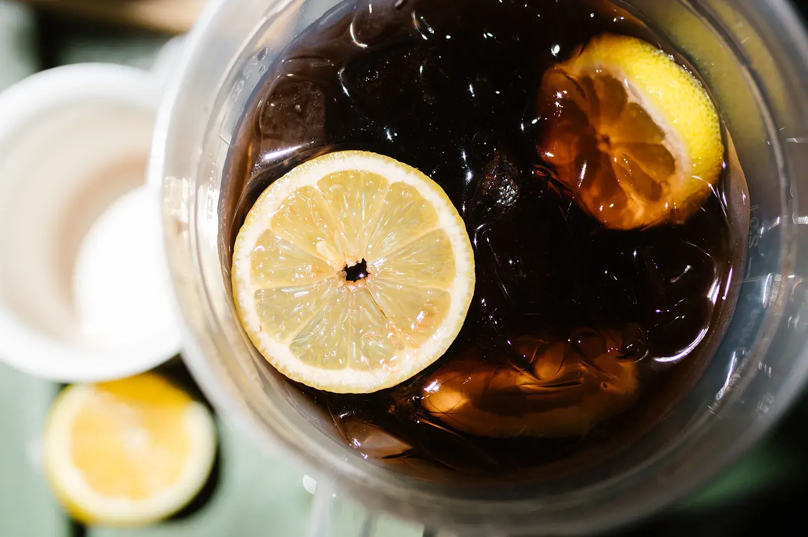 Top-down view of a clear cup filled with dark iced tea, ice cubes, and two lemon slices.