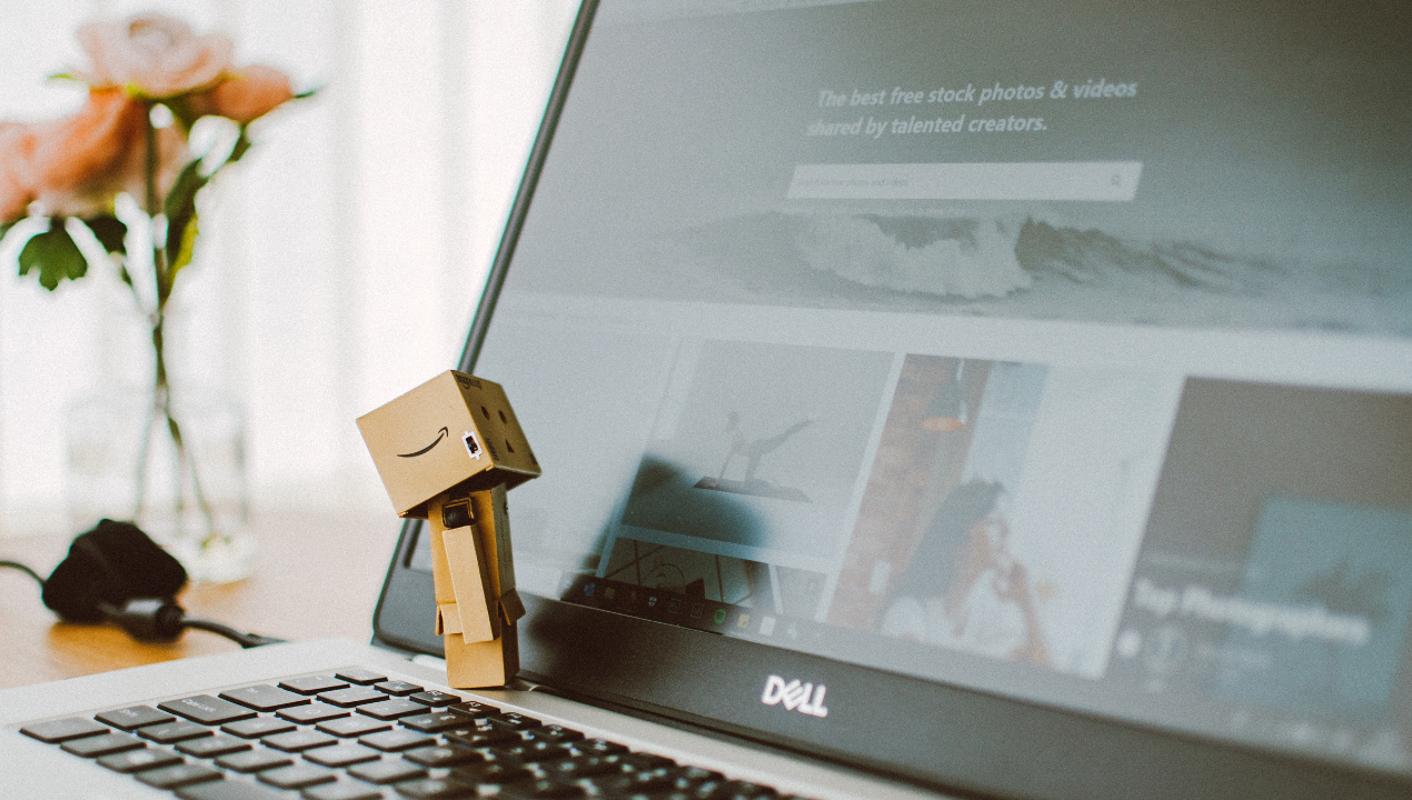 a small cardboard character made from tiny amazon boxes looking at amazon marketplaces on a laptop