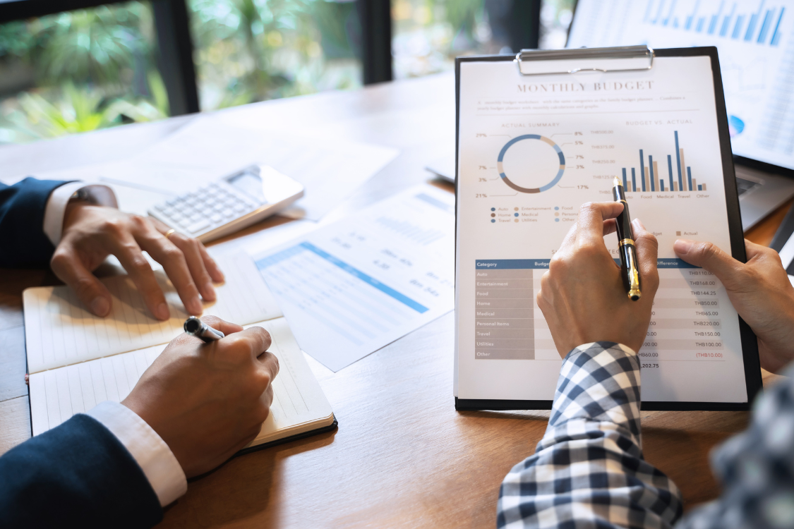 Two professionals discussing financial data on a tablet with charts and documents on the table