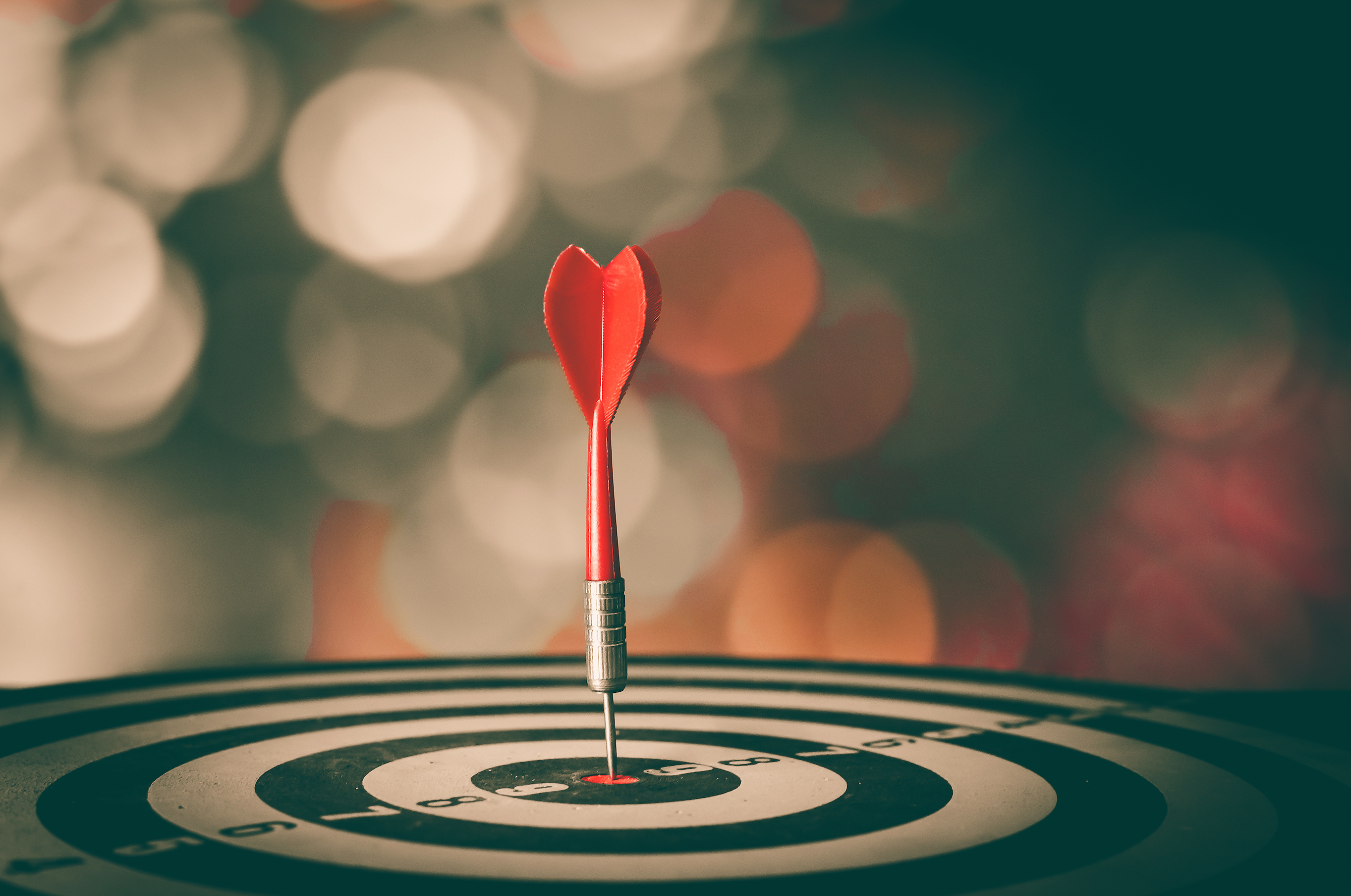 a red dat points down at the bullseye on a black and white dart board against a blurred background