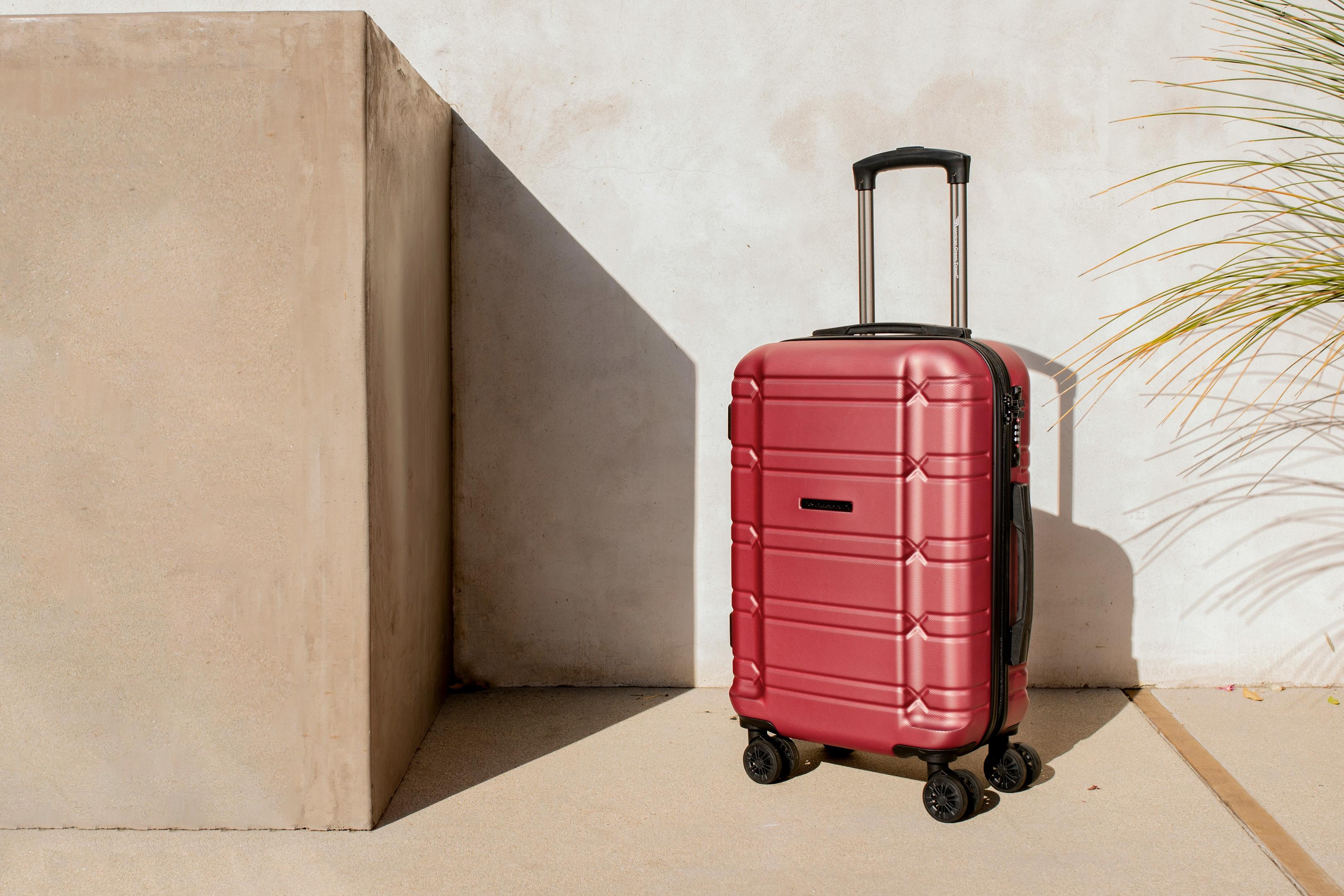 Red hardside spinner polypropelene suitcase standing outdoors against a wall.