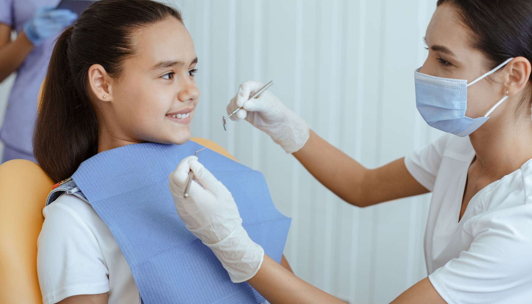 Ising i tennene etter fylling – Hva er normalt? 5 Smilende jente i tannlegestol får tenner undersøkt av tannpleier med munnbind og hansker, i et lyst og trygt klinikkmiljø.