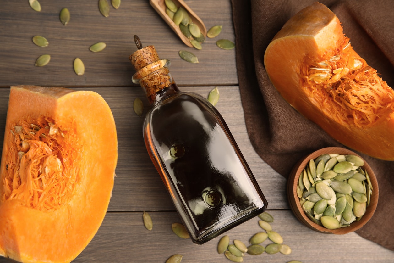 Pumpkin seed oil in dark glass bottle with fresh pumpkin halves and raw pumpkin seeds on rustic wooden table