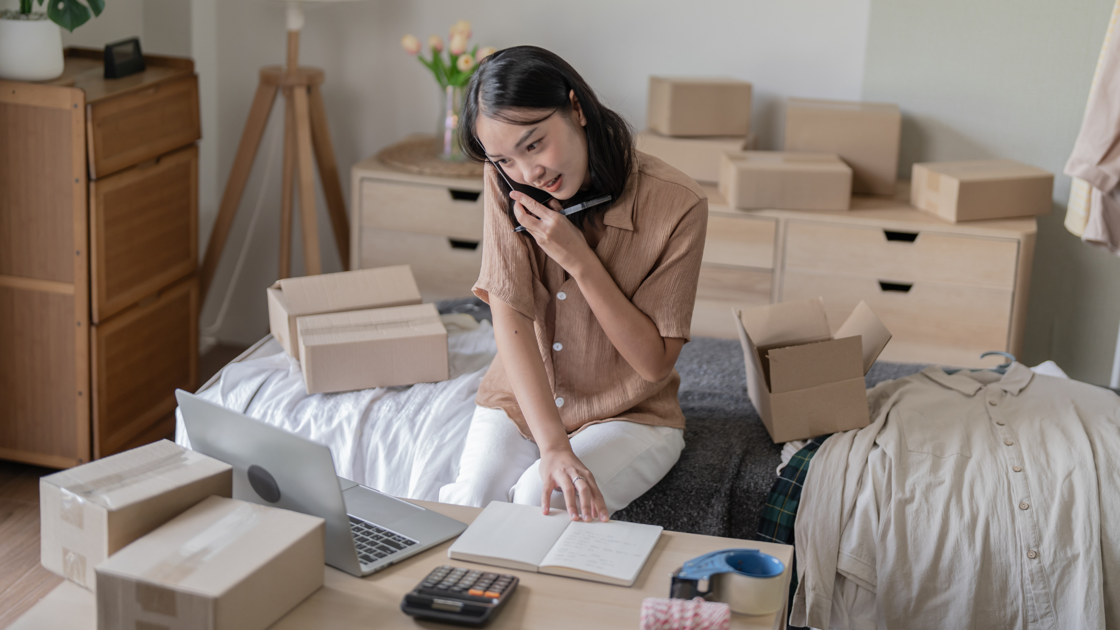 Woman multitasking on a phone call and laptop among boxes, illustrating a flexible South Texas VoIP work setup.