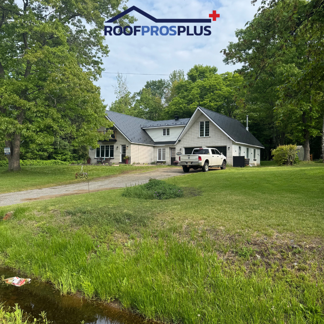 A white house with a black metal roof is surrounded by lush green trees and grass. A white truck is parked in the driveway. 