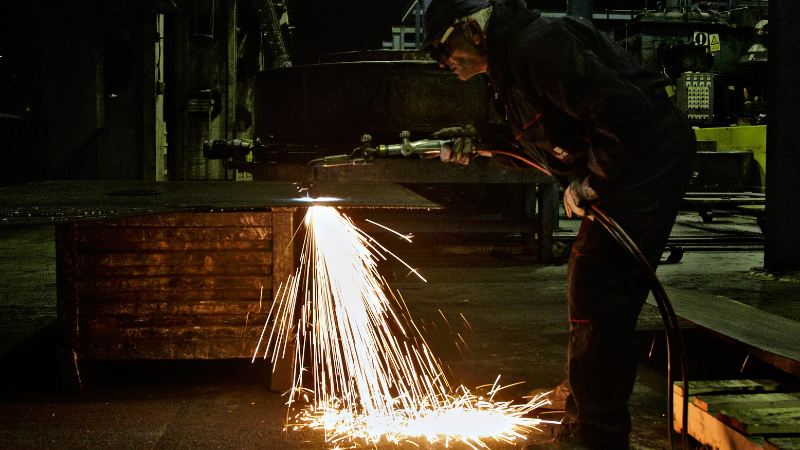 A worker is using flame cutting tech to cut thick metals.