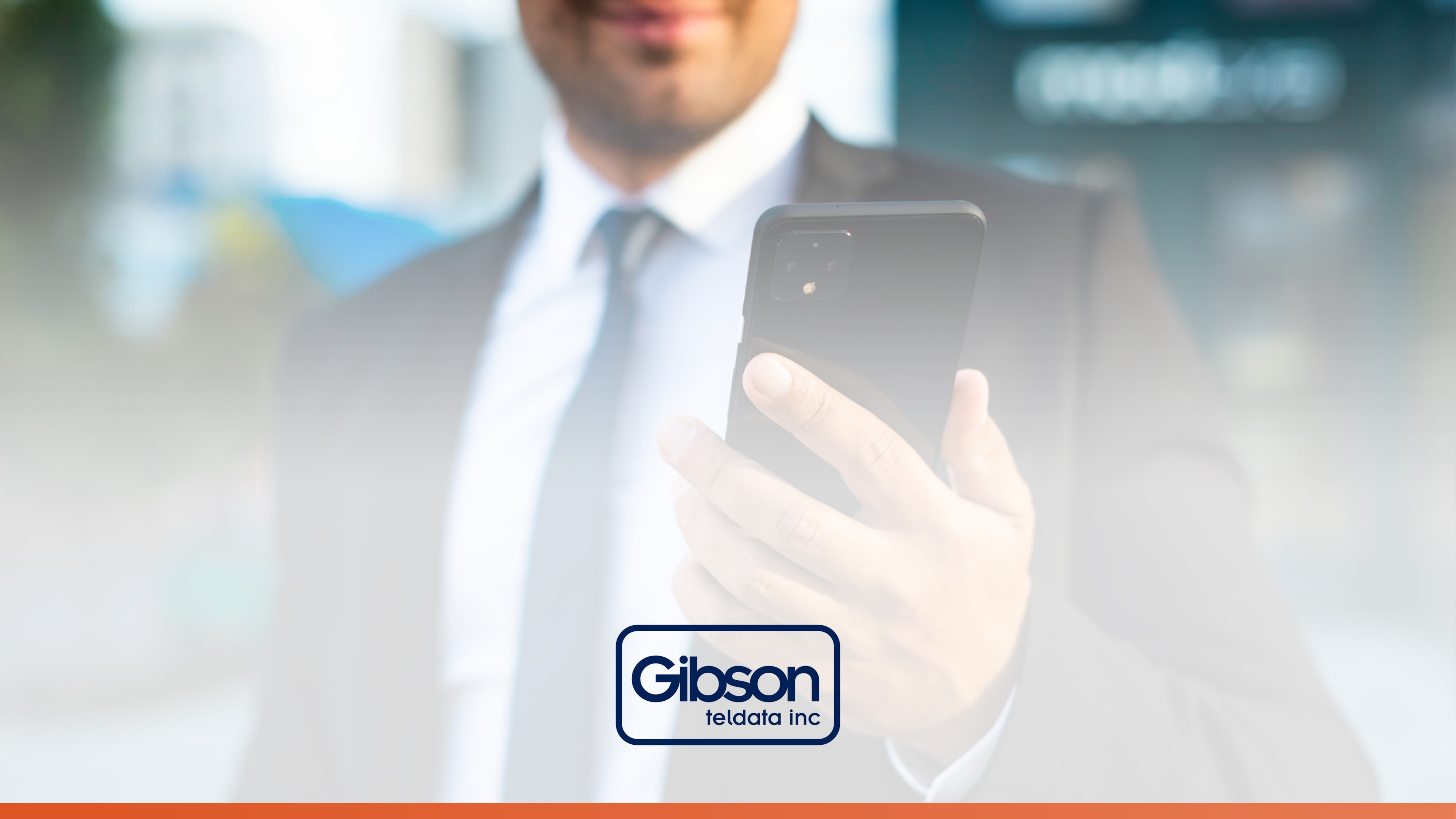 Close-up of a man in a suit holding a smartphone with the Gibson Teldata logo below. Represents Unified Communications technology for seamless business connectivity.