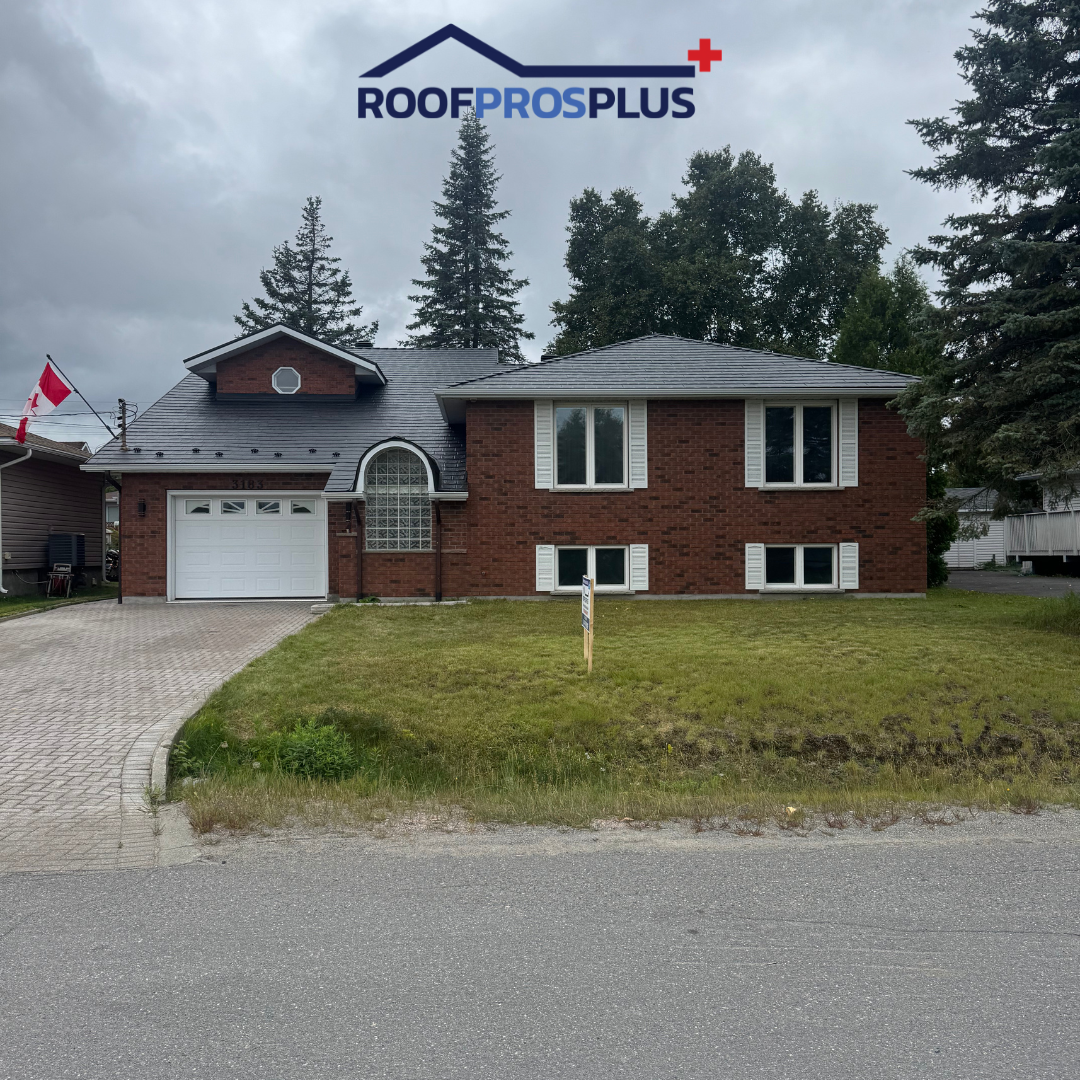 A brick house with a grey metal roof, large windows, and a garage. A Canadian flag hangs from the house on the left-hand side. The "RoofProsPlus" logo is at the top of the image.