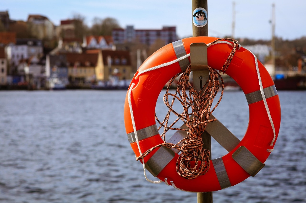 A bright orange life buoy with a coiled rope, mounted near a waterfront, ready for emergency rescues.