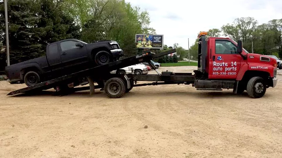 A tow truck hauling a junk car away from a junkyard