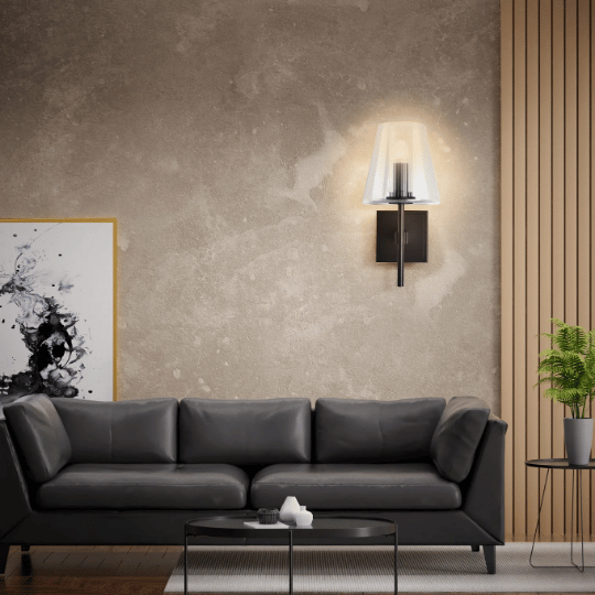 Modern living room with a black leather sofa and minimalist decor, featuring a sleek wall sconce with a translucent shade casting warm ambient light against a textured beige wall.