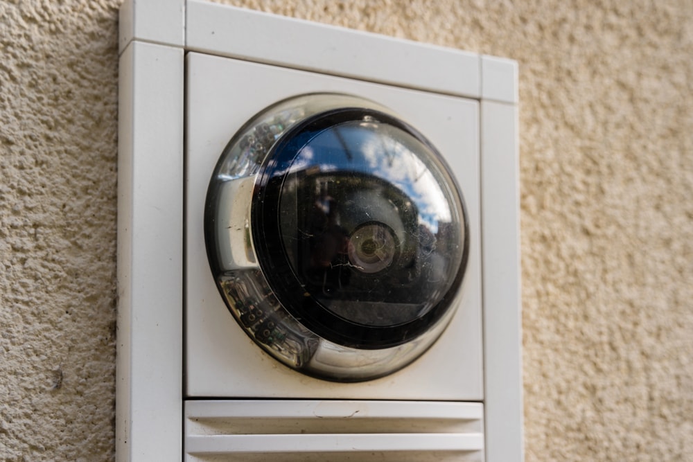 Снимка на камера тип "рибешко око" с бяла рамка монтирана на стена с грапава бежова мазилка